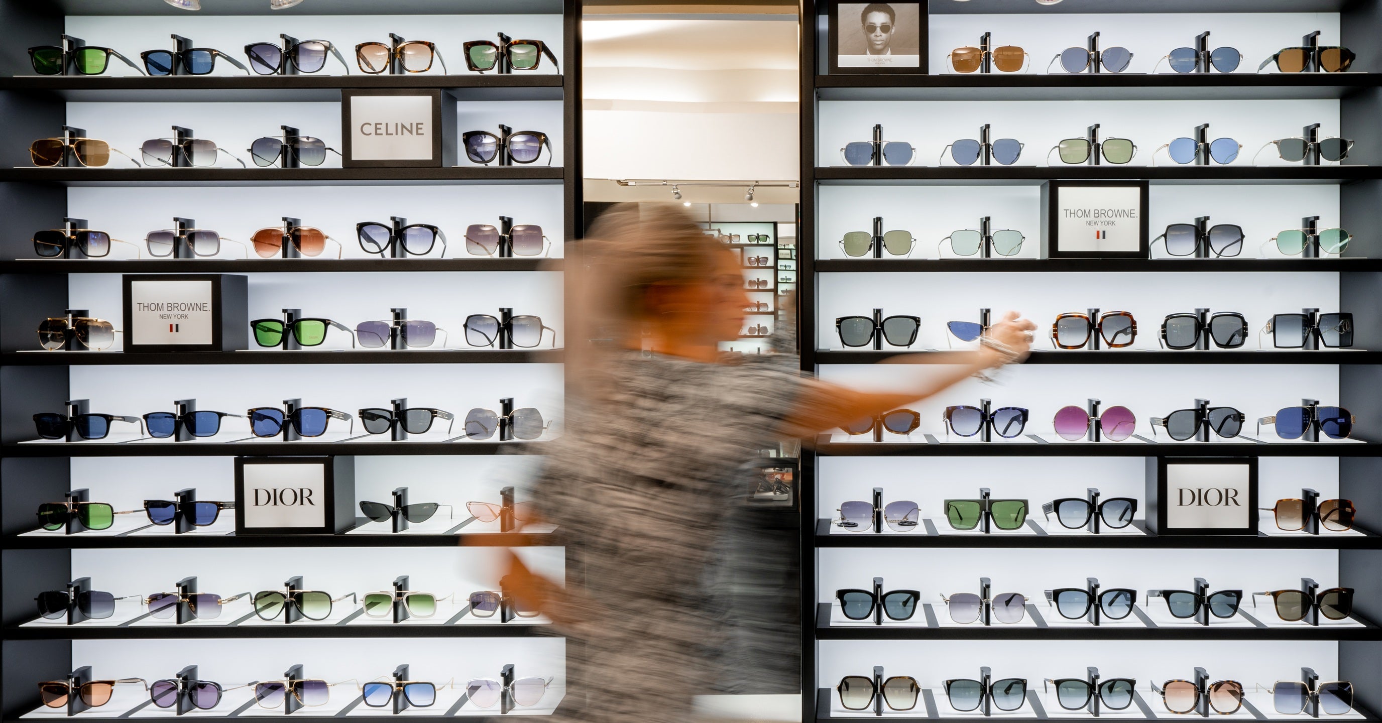 Person browsing through a display of sunglasses in a store with interior optician